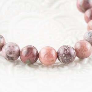 May include: A pink and white gemstone bracelet with round beads. The beads have a mottled pattern.