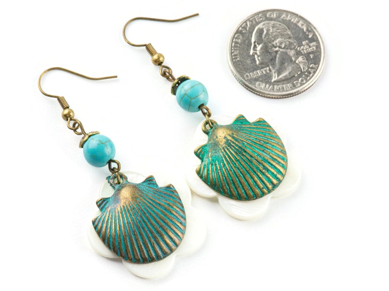 May include: A pair of turquoise and green shell earrings with a white shell accent. The earrings are made with bronze-coloured metal and have a hook closure.