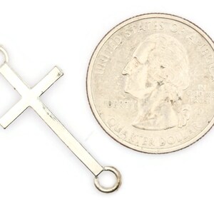 May include: Silver-toned metal cross charm with two jump rings. The charm is about the size of a US quarter.