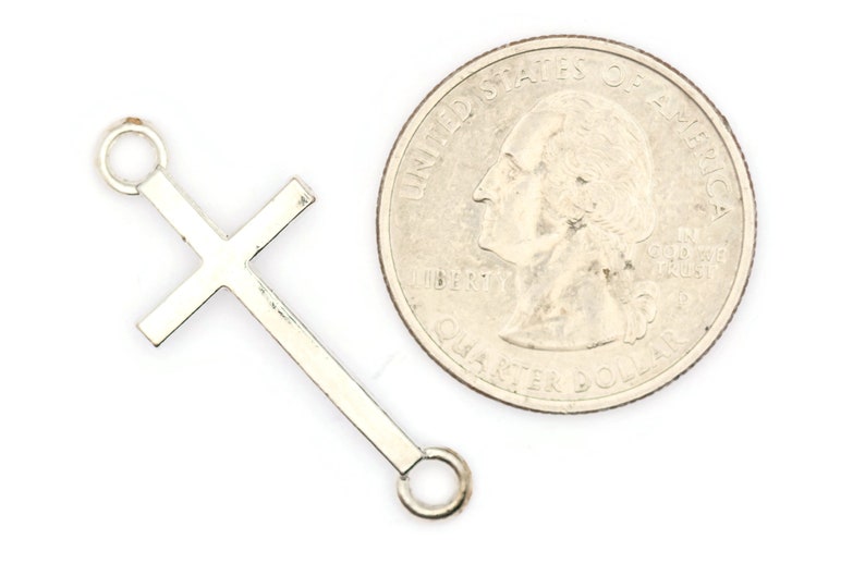 May include: Silver-toned metal cross charm with two jump rings. The charm is about the size of a US quarter.