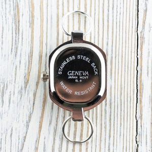 May include: A Geneva watch with a stainless steel back, water resistant, and Japan Movt CL-8. The watch is brown with a silver-colored bezel and two key rings.