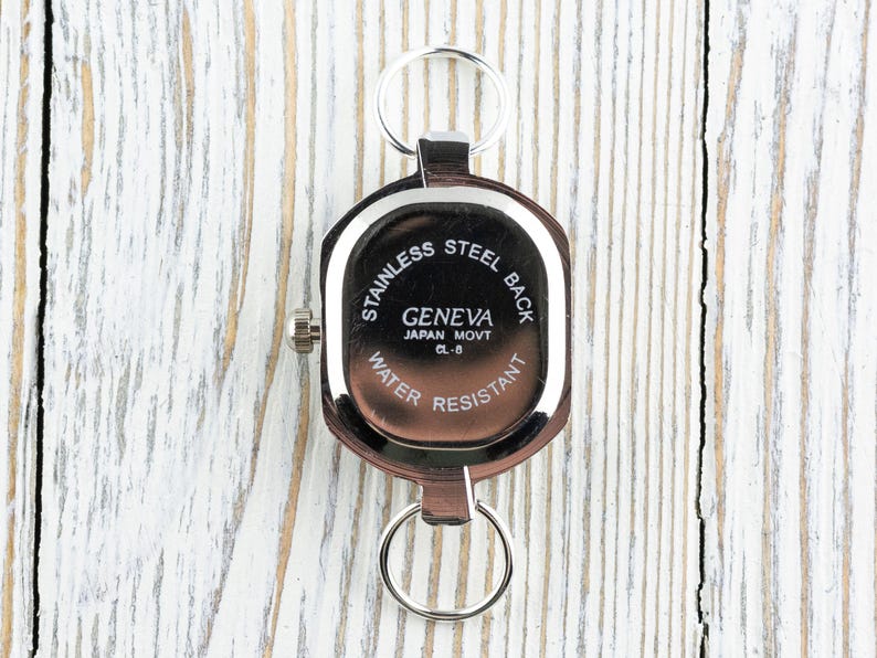 May include: A Geneva watch with a stainless steel back, water resistant, and Japan Movt CL-8. The watch is brown with a silver-colored bezel and two key rings.