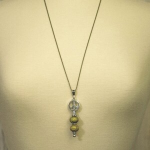 Puede incluir: Un collar de cadena de plata con un dije de signo de paz y tres cuentas doradas.