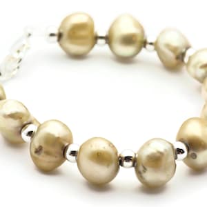 以下が含まれることがあります： シルバーのアクセントが付いたパールブレスレット。パールは薄い金色で、シルバーのチェーンに繋がっています。