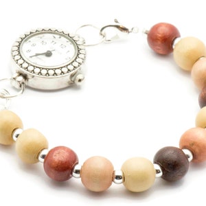 Puede incluir: Un reloj plateado con una esfera redonda y un bisel de cuentas. El reloj est&aacute; unido a una pulsera hecha de cuentas de madera en tonos marrones, beige y rosa.