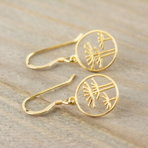 May include: A pair of gold-toned earrings with a delicate design of three trees inside a circle. The earrings have a simple hook closure.