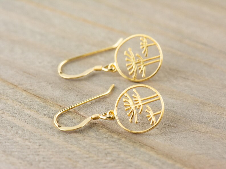 May include: A pair of gold-toned earrings with a delicate design of three trees inside a circle. The earrings have a simple hook closure.