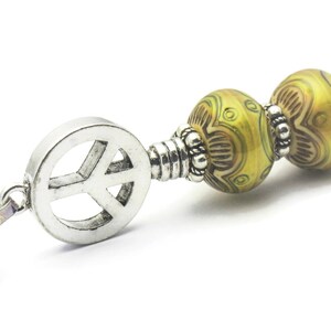 Puede incluir: Un collar con un dije de plata con el signo de la paz y dos cuentas de vidrio con patrones verdes y marrones.