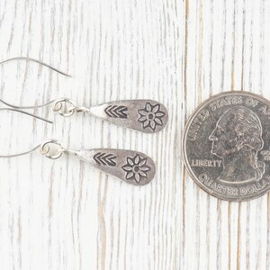 Puede incluir: Un par de pendientes de plata con dise&ntilde;o de flor. Los pendientes son del tama&ntilde;o de una moneda de veinticinco centavos.