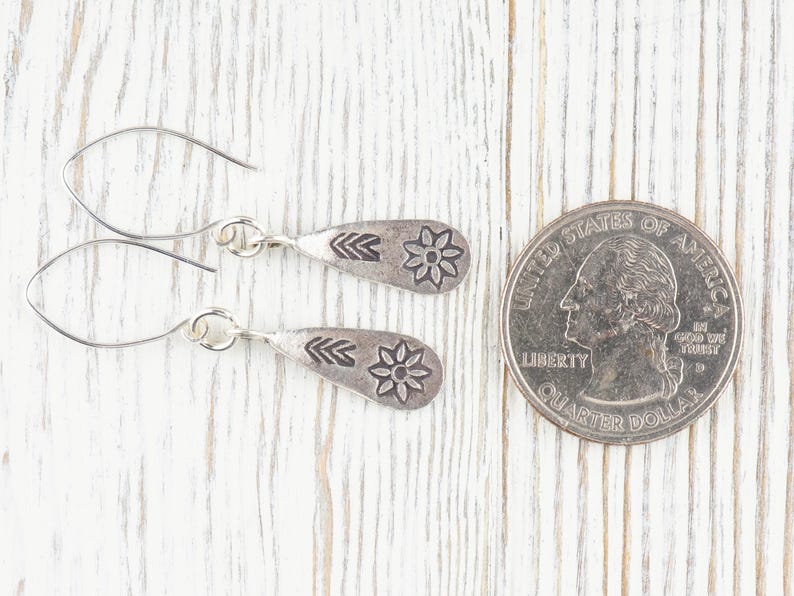 Puede incluir: Un par de pendientes de plata con dise&ntilde;o de flor. Los pendientes son del tama&ntilde;o de una moneda de veinticinco centavos.