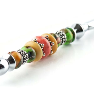 May include: A silver letter opener with a handle decorated with colourful beads. The beads are green, yellow, and orange with a silver accent.