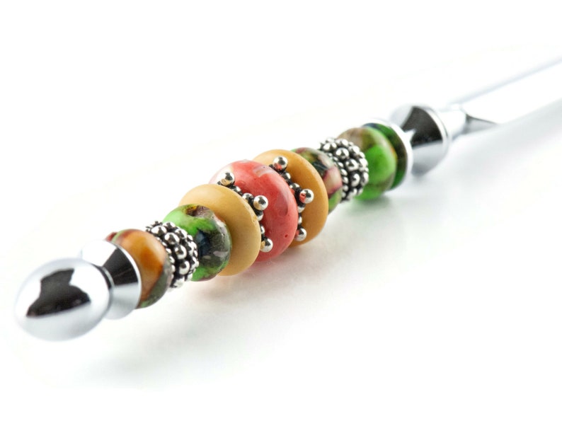 May include: A silver letter opener with a handle decorated with colourful beads. The beads are green, yellow, and orange with a silver accent.
