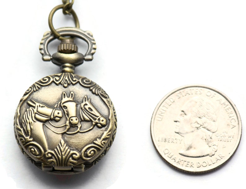 Puede incluir: Reloj de bolsillo antiguo de color dorado con un dise&ntilde;o de tres cabezas de caballo en la parte delantera. El reloj es aproximadamente del tama&ntilde;o de una moneda de 25 c&eacute;ntimos de euro.
