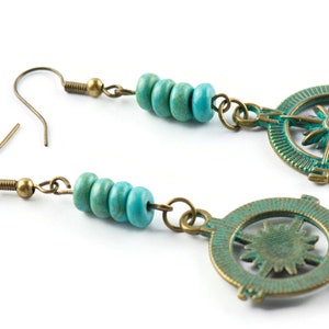May include: A pair of turquoise and bronze earrings featuring a compass design. Each earring has a cluster of turquoise beads and a circular compass charm with a starburst design.