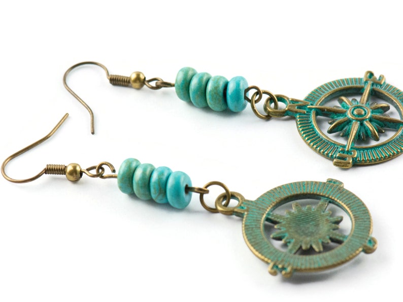 May include: A pair of turquoise and bronze earrings featuring a compass design. Each earring has a cluster of turquoise beads and a circular compass charm with a starburst design.