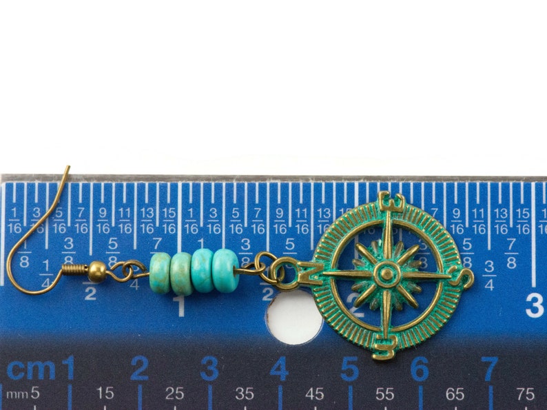 May include: A pair of turquoise and gold earrings with a compass charm. The earrings are approximately 3 cm long and feature a gold hook and a chain with turquoise beads.