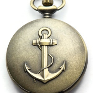 May include: A gold-toned pocket watch with an anchor design on the face. The watch has a chain attached to the top.
