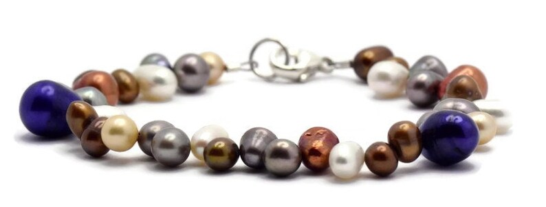 May include: A multi-colored pearl bracelet with a silver clasp. The bracelet features a variety of pearl shapes and sizes, including round, oval, and teardrop. The pearls are in shades of white, cream, brown, and purple.