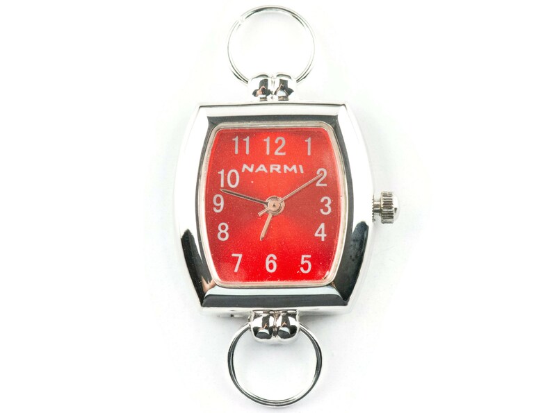 May include: A silver watch with a red face and white numbers. The watch has a square face with rounded corners and a silver band. The watch is attached to a silver chain with a ring at the top.