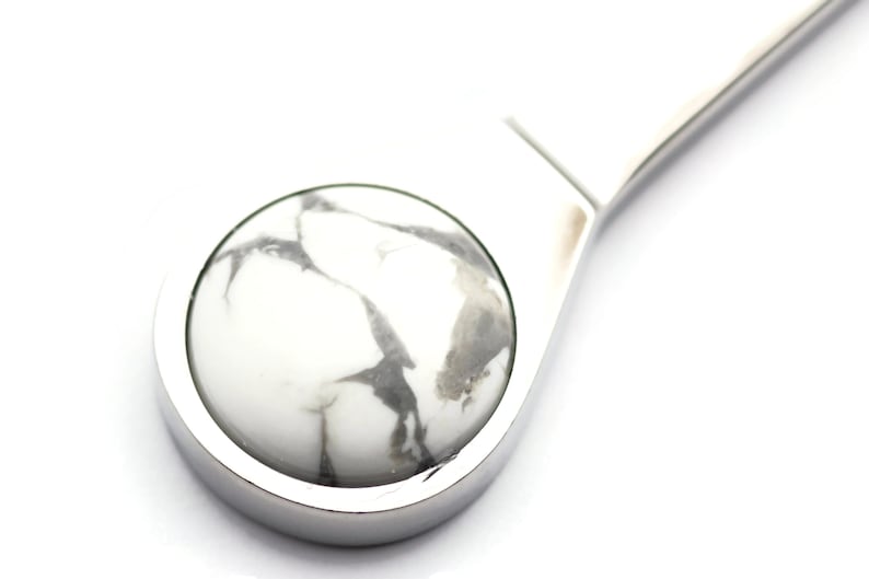 May include: A silver bottle stopper with a white and grey marbled stone top.
