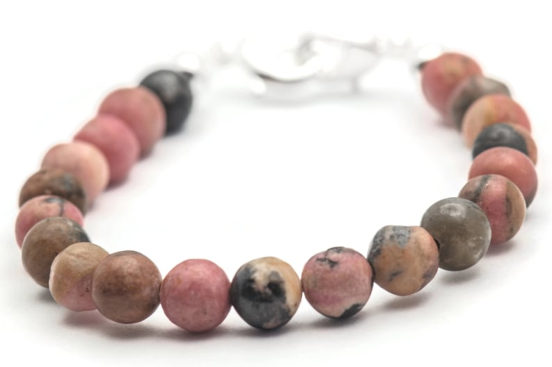 K&ouml;nnte beinhalten: Ein Armband aus rosafarbenen und braunen Edelsteinen mit einem silbernen Verschluss. Das Armband besteht aus runden Perlen und ist etwa 18 cm lang.