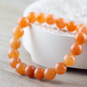 May include: A bracelet made of orange carnelian beads. The beads are round and smooth, and the bracelet is strung on a clear elastic cord.