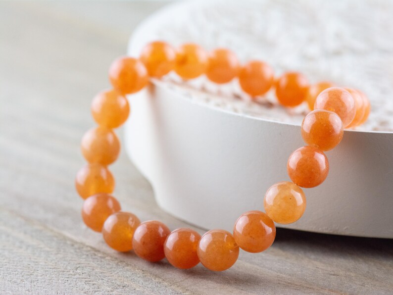 May include: A bracelet made of orange carnelian beads. The beads are round and smooth, and the bracelet is strung on a clear elastic cord.