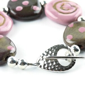 May include: A bracelet made of brown and pink ceramic beads with a silver clasp. The beads are decorated with pink polka dots and swirls.