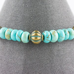 May include: A turquoise and gold beaded bracelet with decorative metal accents. The bracelet is made with round turquoise beads and gold metal beads with a textured design.