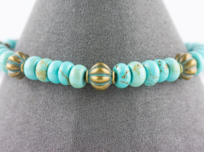 May include: A turquoise and gold beaded bracelet with decorative metal accents. The bracelet is made with round turquoise beads and gold metal beads with a textured design.