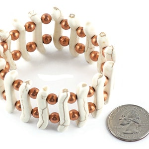 May include: A white and copper beaded bracelet with a stretchy band. The bracelet is about the size of a quarter.
