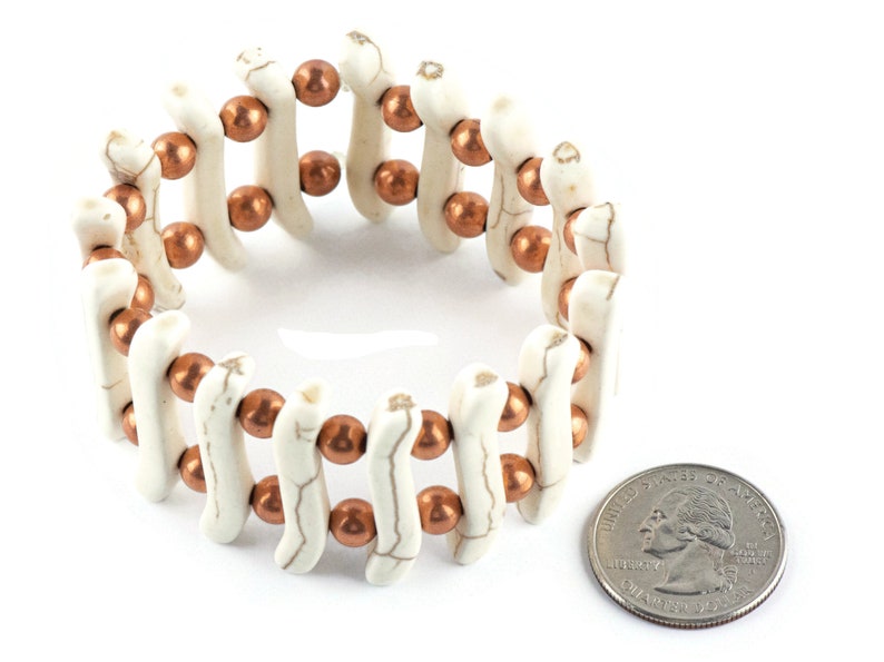 May include: A white and copper beaded bracelet with a stretchy band. The bracelet is about the size of a quarter.