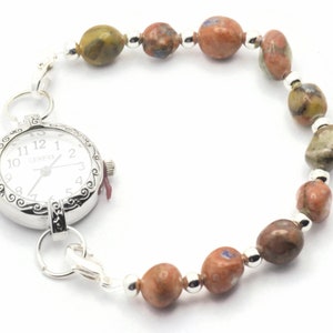 May include: A silver watch with a white face and black numbers is attached to a bracelet made of brown, green, and white stones.
