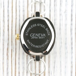 Peut inclure: Une montre Geneva argent&eacute;e avec un cadran noir et une couronne dor&eacute;e. La montre a un dos en acier inoxydable et est r&eacute;sistante &agrave; l'eau. La montre est attach&eacute;e &agrave; un porte-cl&eacute;s argent&eacute;.