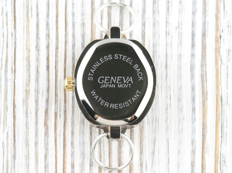 Peut inclure: Une montre Geneva argent&eacute;e avec un cadran noir et une couronne dor&eacute;e. La montre a un dos en acier inoxydable et est r&eacute;sistante &agrave; l'eau. La montre est attach&eacute;e &agrave; un porte-cl&eacute;s argent&eacute;.
