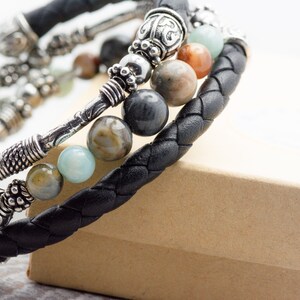 May include: A black leather bracelet with silver accents and multi-colored gemstone beads. The bracelet is wrapped around a brown box.