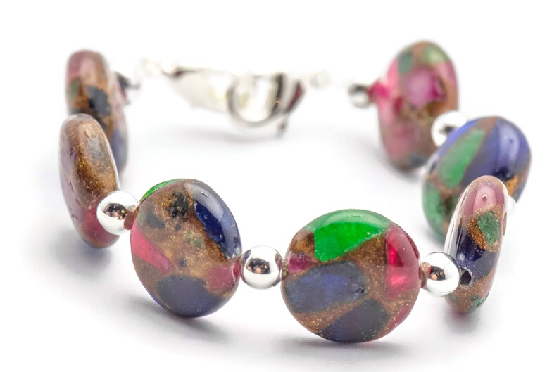 May include: A bracelet made of round, multi-colored glass beads with gold flecks. The beads are a mix of green, blue, red, and brown.