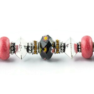 May include: A close-up of a black and red beaded bracelet with a clear crystal bead and a black bead with a floral design.