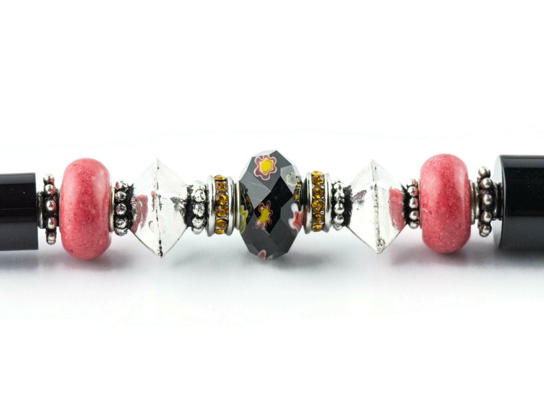 May include: A close-up of a black and red beaded bracelet with a clear crystal bead and a black bead with a floral design.