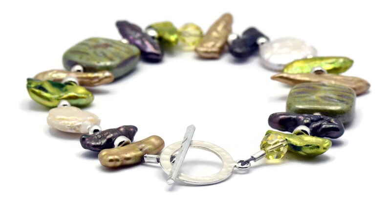 K&ouml;nnte beinhalten: Ein Armband aus gr&uuml;nen, braunen und violetten Perlen mit einem silbernen Schiebeverschluss. Das Armband besteht aus verschiedenen unregelm&auml;&szlig;ig geformten Perlen.