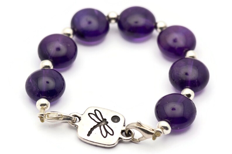 May include: A purple amethyst gemstone bracelet with a silver dragonfly charm. The bracelet is made with round beads and a silver clasp.