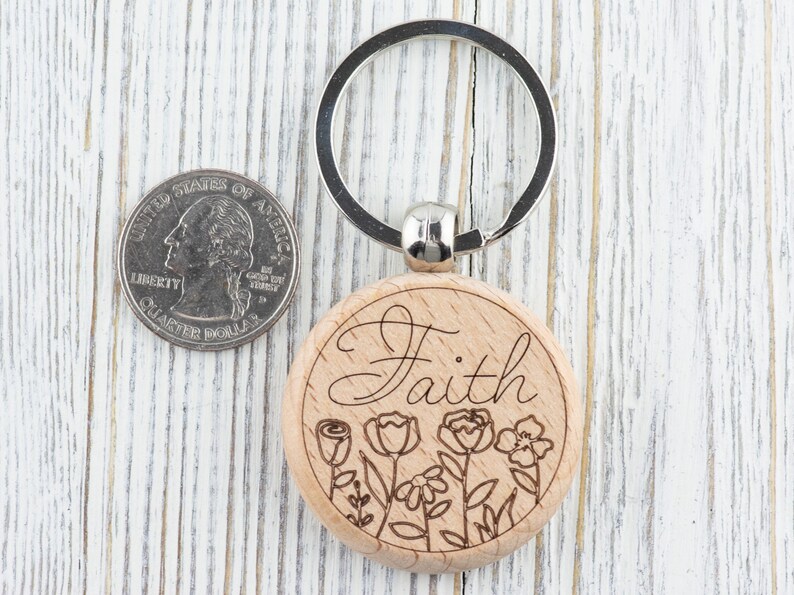May include: Wooden keyring with a silver key ring. The keyring is round and has the word "Faith" engraved on it. The word is surrounded by a floral design.