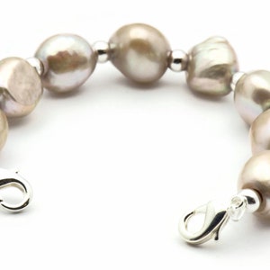 Peut inclure: Un bracelet en perles avec un fermoir argent&eacute;. Les perles sont de couleur gris clair et sont enfil&eacute;es sur une cha&icirc;ne argent&eacute;e.