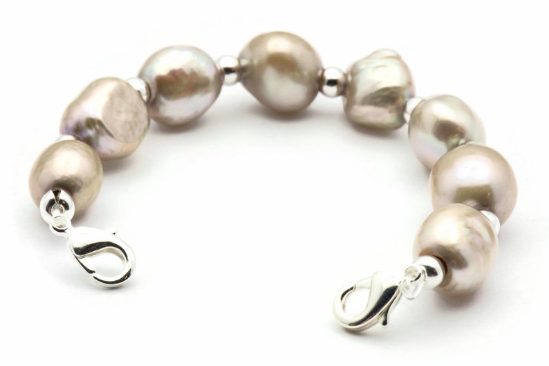 Peut inclure: Un bracelet en perles avec un fermoir argent&eacute;. Les perles sont de couleur gris clair et sont enfil&eacute;es sur une cha&icirc;ne argent&eacute;e.