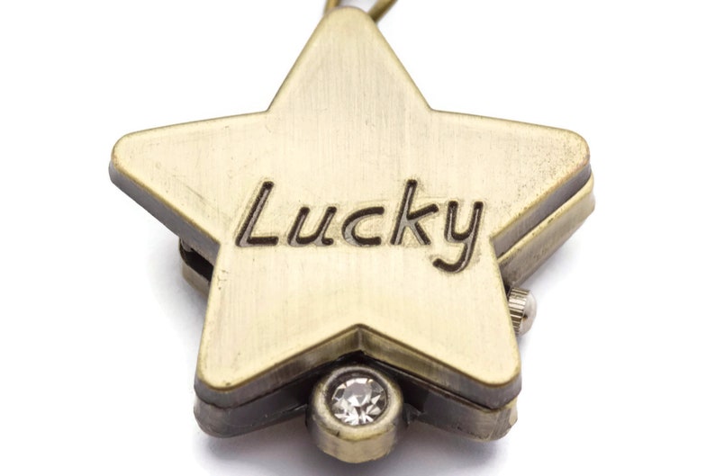 Peut inclure: Un pendentif en forme d'&eacute;toile de couleur or avec le mot "Lucky" grav&eacute; sur le devant. Le pendentif a un petit strass transparent au centre.