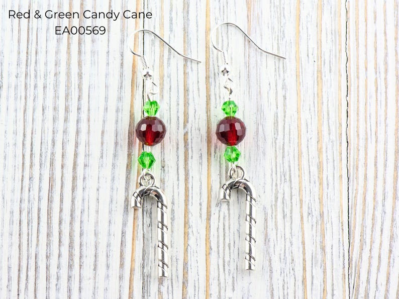Pode incluir: Um par de brincos com tema natalino. Cada brinco apresenta um pingente de bengala doce prateada, contas vermelhas e verdes e um gancho prateado. O texto "Red & Green Candy Cane EA00569" &eacute; vis&iacute;vel na imagem.