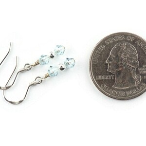 May include: A pair of silver earrings with light blue crystal beads. The earrings are shown next to a US quarter for size comparison.