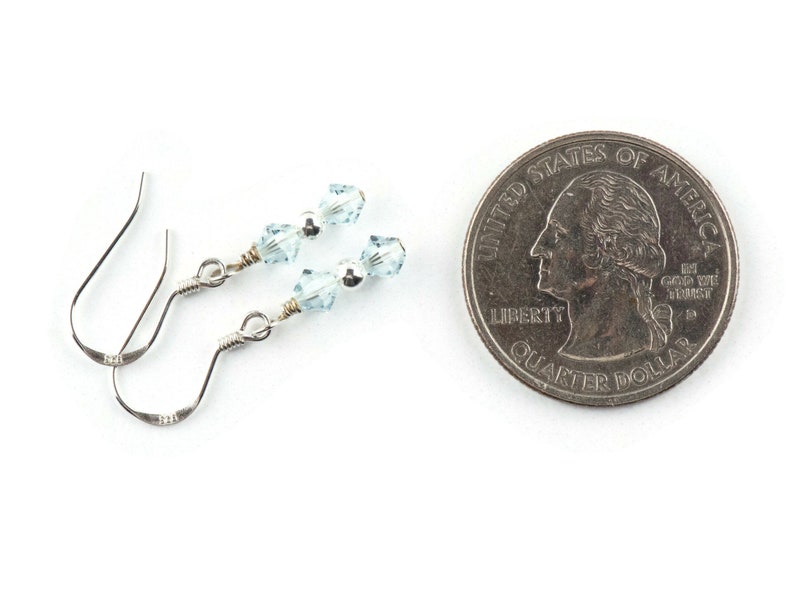May include: A pair of silver earrings with light blue crystal beads. The earrings are shown next to a US quarter for size comparison.
