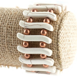 May include: A white and copper bracelet with a woven design. The bracelet is made of white ceramic beads and copper beads.