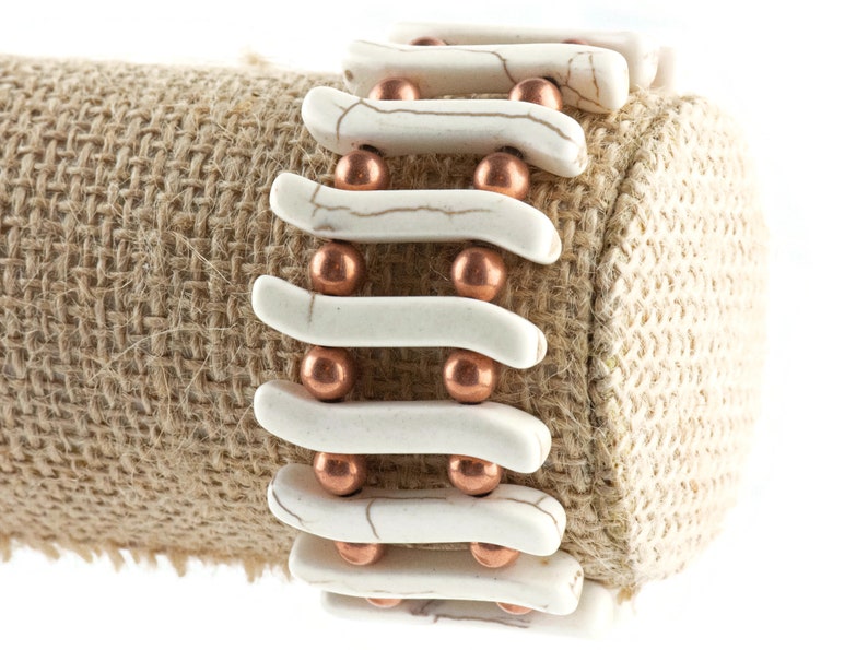 May include: A white and copper bracelet with a woven design. The bracelet is made of white ceramic beads and copper beads.